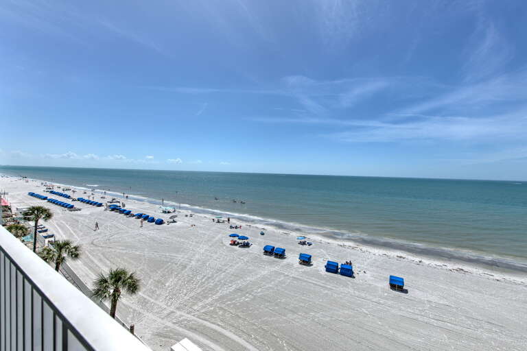 Pristine white sand beach stretches along emerald waters with blue umbrellas and comfortable loungers awaiting guests.