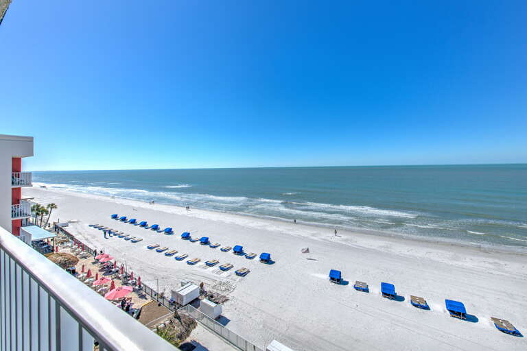 Pristine white sand beach stretches endlessly beneath brilliant blue skies, with organized beach chair rentals and beachfront property visible in the scene.