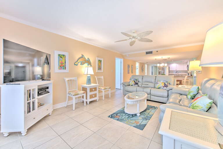 Relax in your bright, coastal-themed living space with comfortable sectional seating, tropical artwork, and modern entertainment center.
