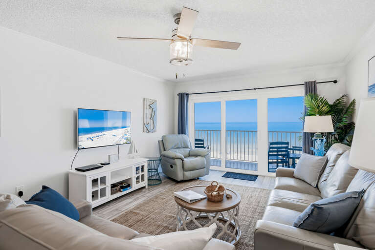 Your coastal living room opens to stunning ocean views through glass doors, while you relax on plush seating with entertainment at your fingertips.