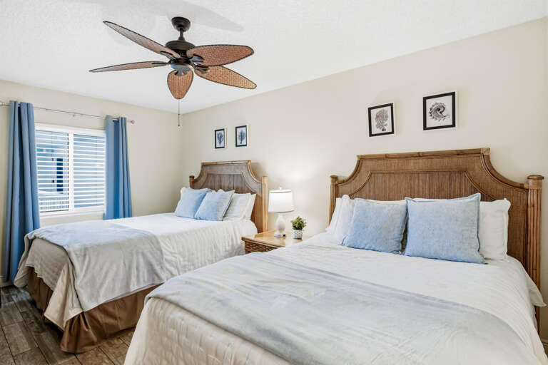 Rest easy in your coastal-themed bedroom with two comfortable beds, tropical ceiling fan, and peaceful blue accents creating the perfect retreat.