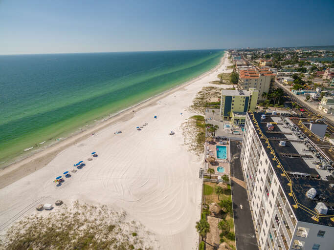 Aerial view showcasing pristine white sand beaches meeting turquoise Gulf waters, with beachfront hotels and coastal community nearby.