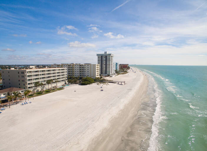 Aerial view showcases pristine white sand beach stretching along turquoise waters, with oceanfront hotels and condominiums lining the shore.