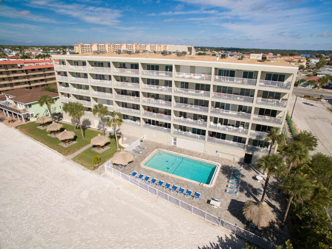Beachfront property featuring multi-story building with private balconies, sparkling pool, and tropical palm trees in sunny coastal setting.