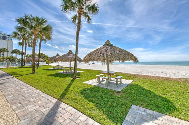 Beautiful beachfront area with thatched umbrella seating and pristine white sand stretching to turquoise waters.