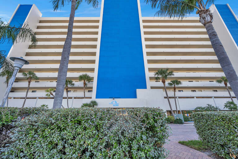 Modern beachfront hotel with distinctive blue and white architecture surrounded by swaying palm trees.