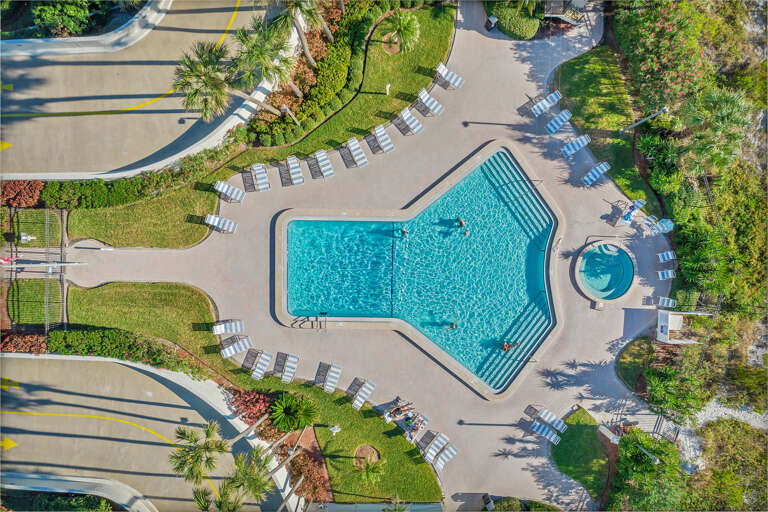 Aerial view of the resort-style pool complex with expansive deck area, spa, and tropical landscaping throughout the property grounds.