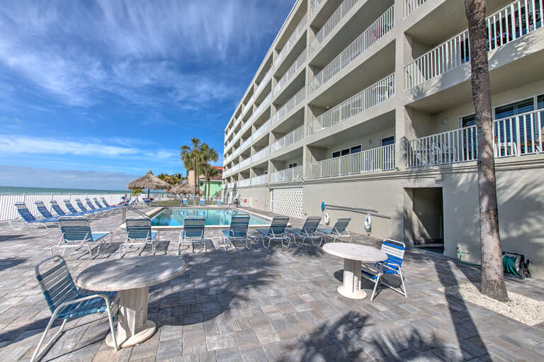 Multi-story beachfront property featuring an outdoor pool deck with lounge chairs and dining tables, steps from the sandy shore.