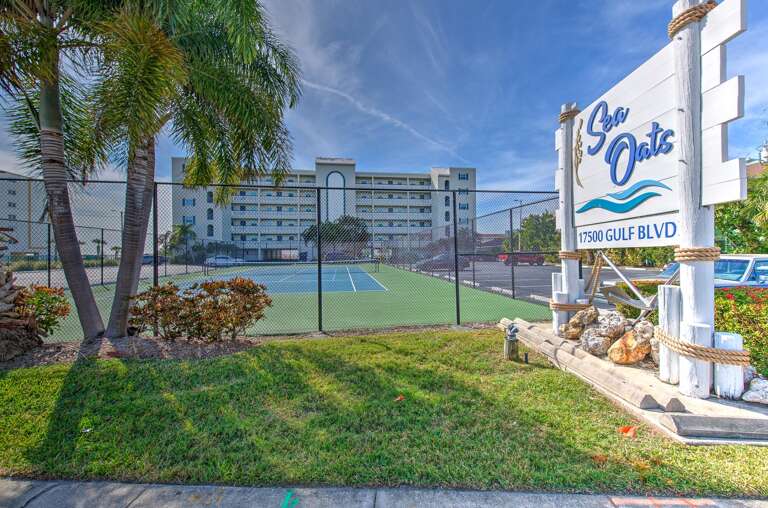 Sea Oats resort entrance welcomes guests to coastal comfort with tennis courts and tropical landscaping along Gulf Boulevard.