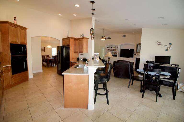 Spacious Kitchen Leading Into Dining Area With Beige Floors And Black Furniture