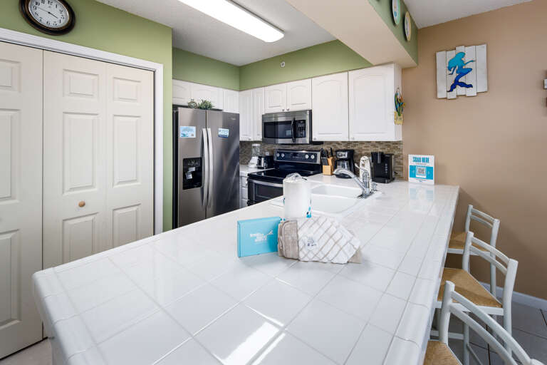 The kitchen of this one-bedroom unit has several nice features, including tiled countertops, Mr. Coffee and Keurig coffee makers and two-sided sink with pull out sprayer. 3 chairs at the island provide additional seating