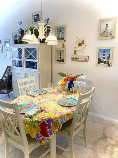 Brightly-lit Dining Space With White Walls, Framed Photos, And A Vibrant Tablecloth