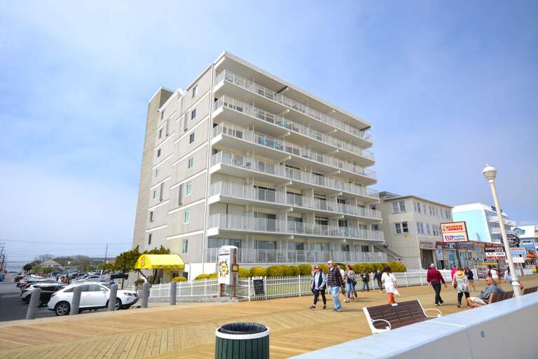 Large Building By Bustling Boardwalk, People Walking Beneath Blue Sky
