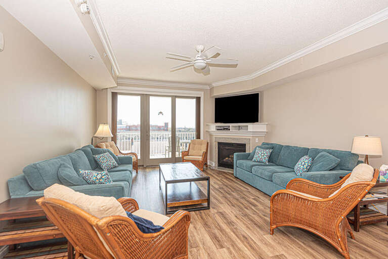 Spacious Living Area With Sofas, Wicker Chairs, And Wood Flooring, Leading To A Balcony