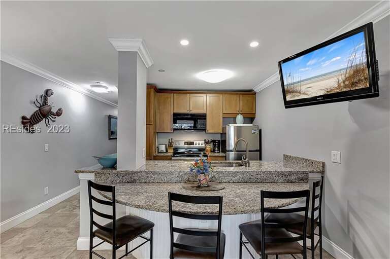 Interior Kitchen And Dining Area With Bar Stools And Mounted TV