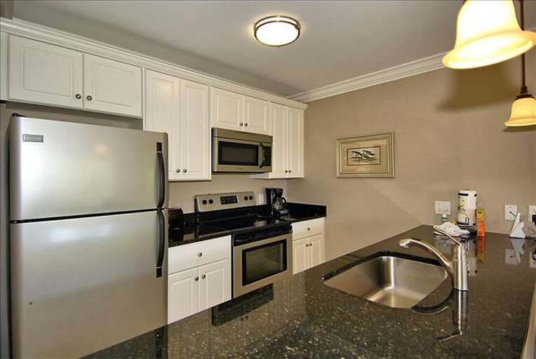 Completely furnished kitchen that looks to dining area and oceanfront view.