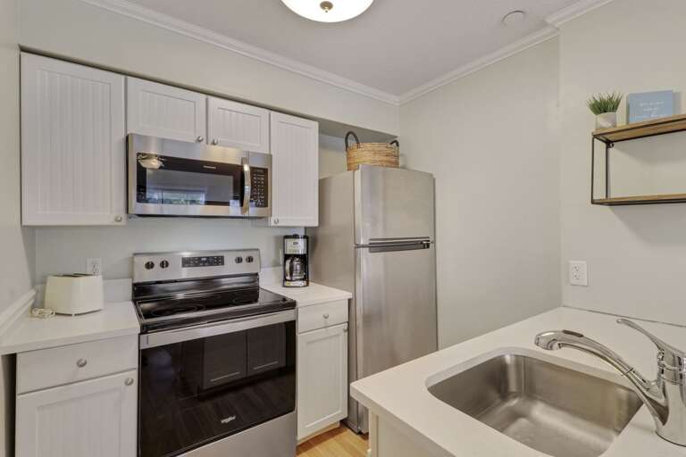 New appliances and countertops in this bright, white kitchen.  Standard coffeemaker. 