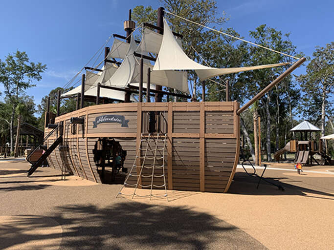 Wooden Ship-shaped Playground Structure With Slides And Climbing Nets Under Bright Blue Sky