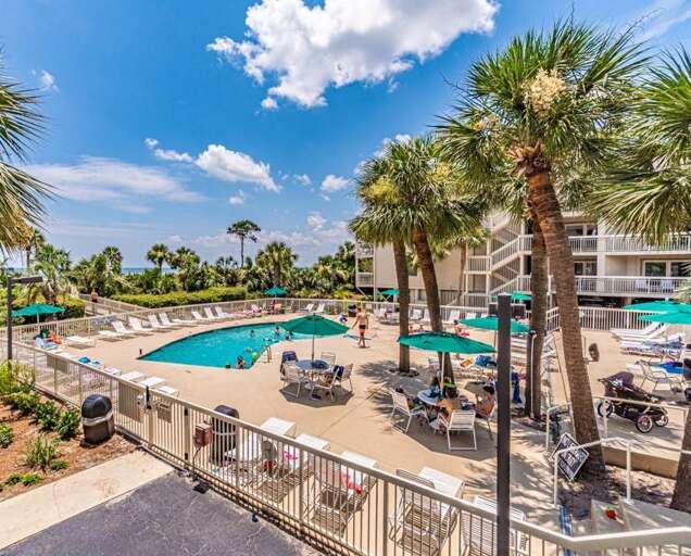 Swimming Pool Area With Loungers And Palm Trees At Vacation Rental Complex