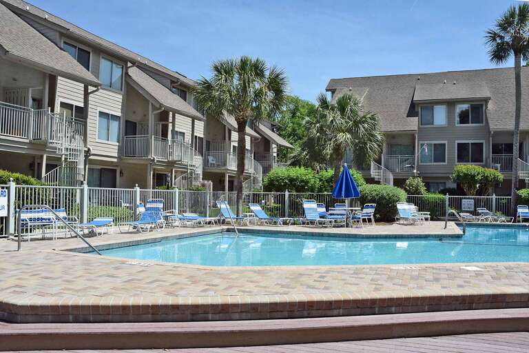 Swimming Pool With Surrounding Buildings And Deck Chairs