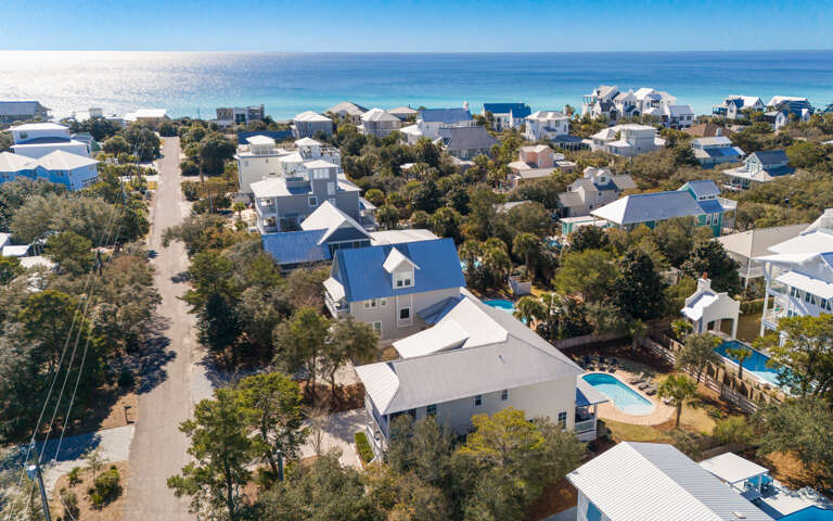 Aerial view of a charming coastal neighborhood with vacation homes nestled among trees, just steps from pristine beaches.