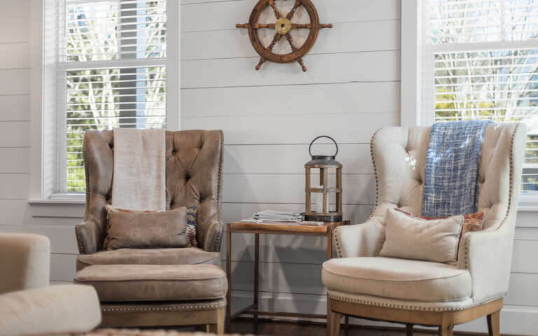 Sink into plush wingback chairs by bright windows where natural light and coastal charm create your perfect reading retreat.