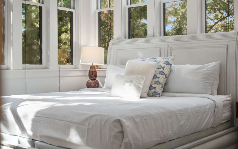Wake up to sunlight streaming through expansive windows, creating your perfect morning sanctuary with crisp linens and peaceful tree views.