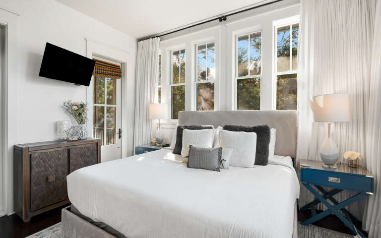 Unwind in your elegant bedroom with crisp white linens, natural light streaming through French doors, and modern amenities for ultimate comfort.