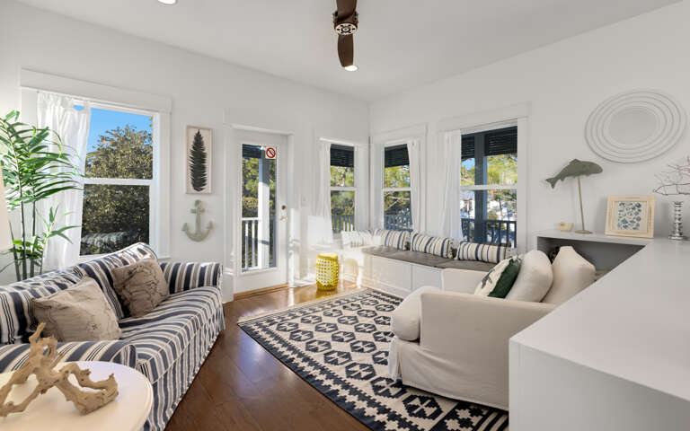 Relax in your bright coastal living room with nautical touches, built-in window seating, and views of lush greenery.