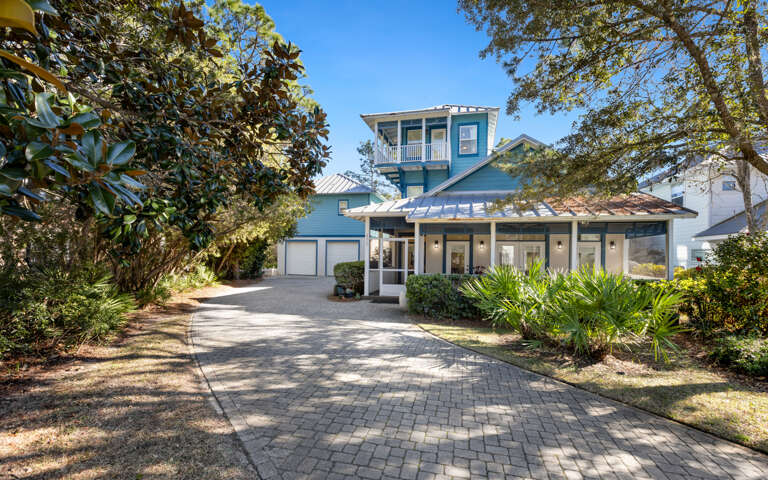 Charming coastal home with lush landscaping and brick-paved driveway creates a welcoming arrival experience in this peaceful neighborhood setting.