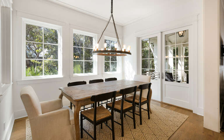 Gather around this elegant dining table where warm conversations flow beneath the rustic chandelier, with garden views framing every meal.