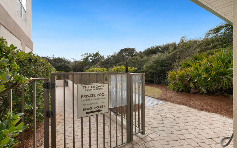 The Legacy Condominiums entrance gate leads to private pool and beach access amid lush tropical landscaping.
