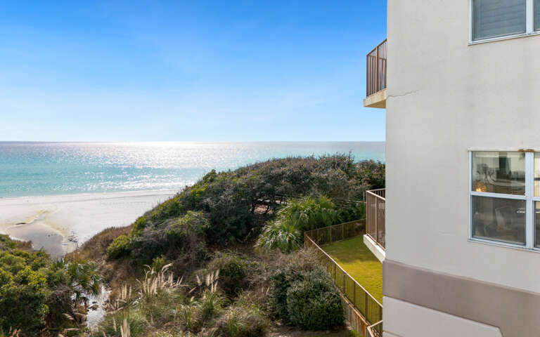 Modern gulf front property overlooks pristine white sand and turquoise waters through lush coastal dunes.