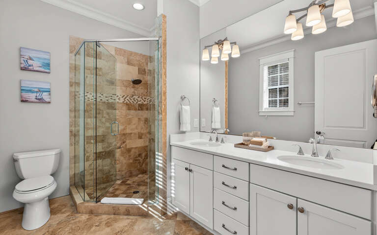 Your spacious bathroom features dual vanities, a luxurious glass-enclosed shower with mosaic accents, and elegant fixtures for your comfort.