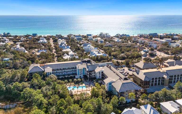 Aerial view of resort property nestled among coastal homes, featuring swimming pool and direct beach access.