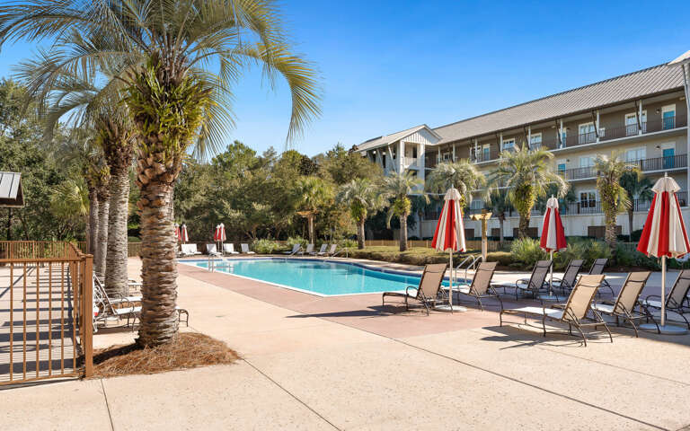 Sparkling pool surrounded by swaying palm trees and comfortable loungers under vibrant red umbrellas—your perfect spot to unwind.
