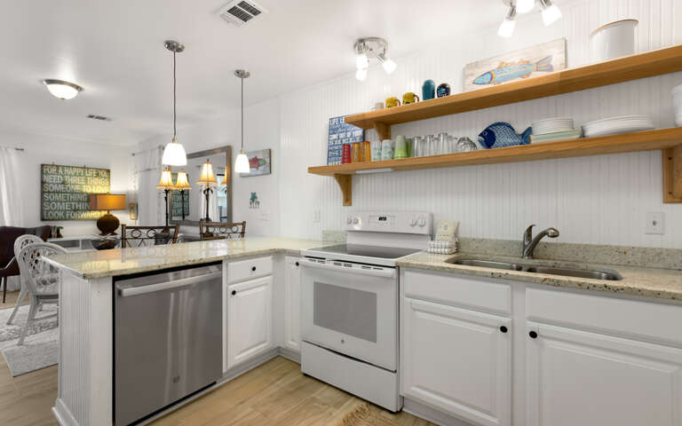 Your bright kitchen features granite counters, stainless appliances, and charming open shelving with coastal touches for your perfect beach getaway.