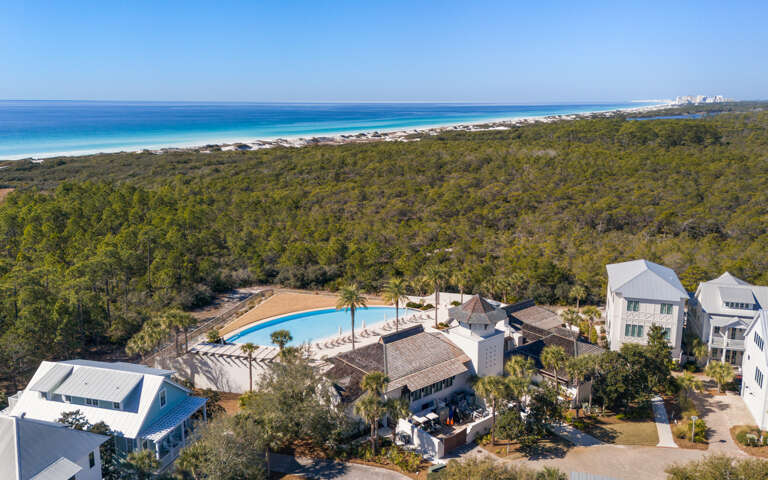 Stunning aerial view of beachfront vacation properties nestled between lush forest and pristine white sand beaches with crystal-clear turquoise waters.