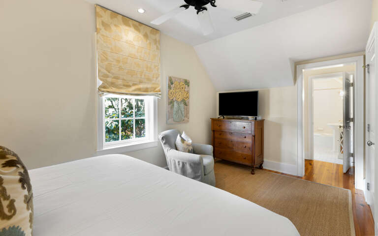 Unwind in your peaceful bedroom featuring a plush reading chair, warm natural light, and entertainment center for cozy evenings.