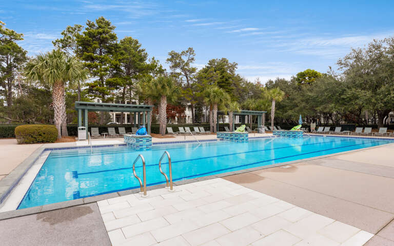 Large community swimming pool surrounded by palm trees and cabanas with lounge seating areas.