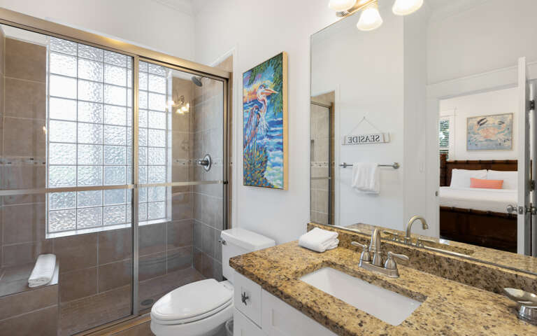 Your private bathroom features a spacious glass shower, granite countertops, and bright coastal artwork that adds charm to your daily routine.