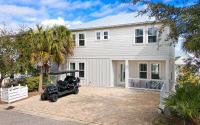 Contemporary two-story beach house with covered parking and tropical landscaping in a coastal neighborhood setting.