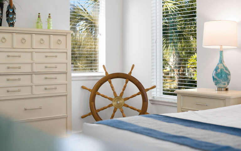 Your coastal bedroom features nautical charm with a ship's wheel centerpiece, tropical views, and soothing ocean-inspired decor.