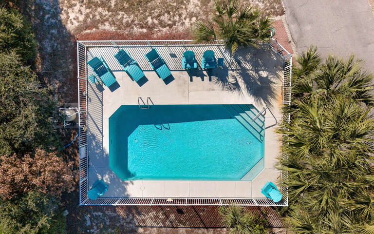Aerial view of a turquoise swimming pool surrounded by palm trees and lounge chairs, perfect for vacation relaxation.