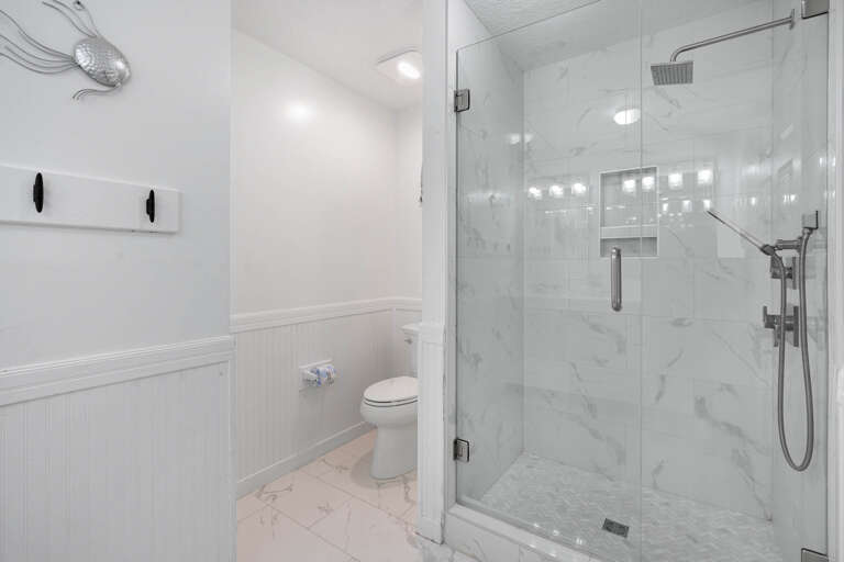 Step into your pristine marble bathroom where elegant white wainscoting meets a luxurious glass-enclosed shower with rainfall showerhead.