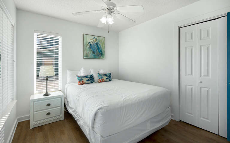 Drift into peaceful sleep in your bright bedroom, complete with fresh linens, tropical artwork, and gentle ceiling fan for perfect comfort.