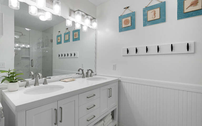 Step into your coastal-themed bathroom featuring dual vanities, elegant lighting, and beachy artwork that creates a spa-like retreat.