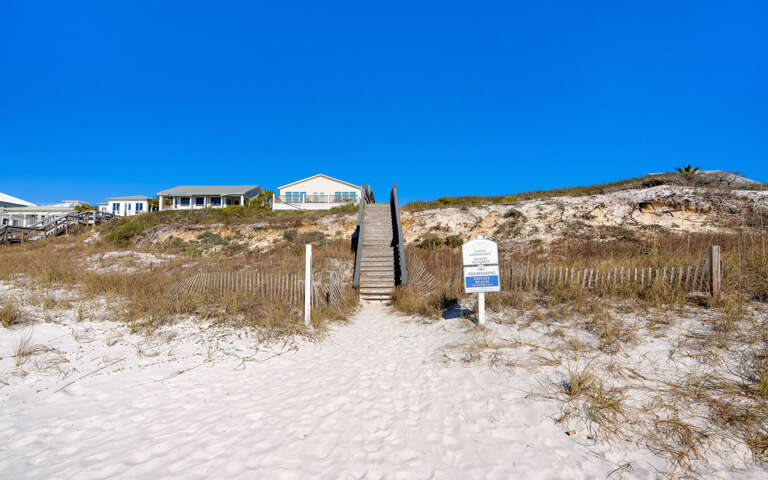 Gulf front vacation homes perched on sandy dunes with direct beach access via wooden boardwalk stairs.