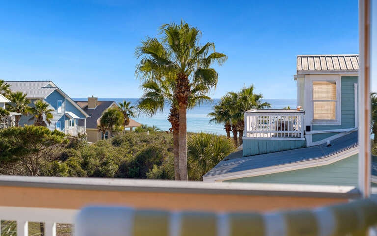 Coastal neighborhood with colorful beach houses and swaying palm trees beneath clear blue skies near the gulf.