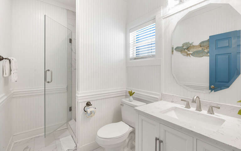 Unwind in your pristine bathroom featuring elegant white marble, a spacious walk-in shower, and charming coastal touches that create a spa-like retreat.